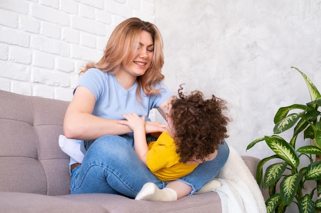 Les jeunes femmes jouent avec sa fille bouclée sur le canapé, elles rient dans leurs bras et s'amusent ensemble