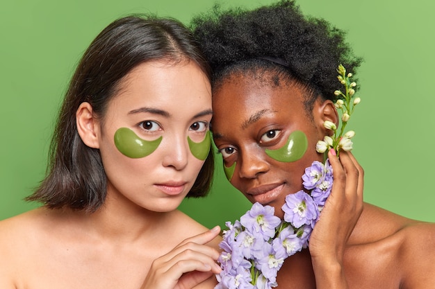 Les jeunes femmes métisses subissent des procédures de beauté appliquent des patchs d'hydrogel sous les yeux tiennent des herbes de fleurs