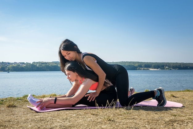 Les jeunes femmes minces faisant des exercices d'étirement se détendre et se réchauffer après le jogging et la course dans le parc près du lac