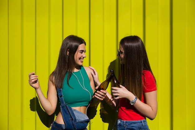 Les jeunes femmes en plein air contre le mur vert écoutent de la musique sur les écouteurs et s'amusent