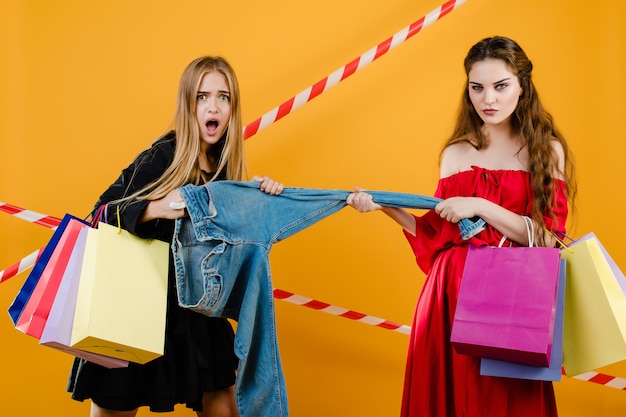 Jeunes Femmes Portant Des Robes Se Disputant Une Paire De Jeans Avec Des Sacs Isolés Sur Jaune