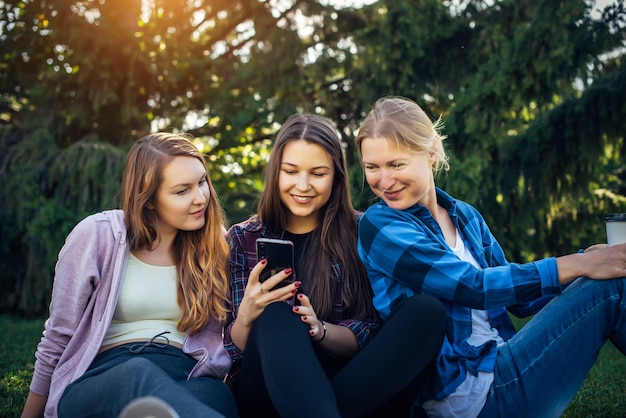 Les jeunes femmes s'asseoir sur l'herbe verte et regarder le smartphone