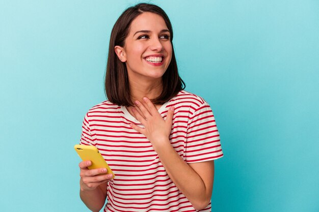 Les jeunes femmes tenant un téléphone portable isolé éclatent de rire en gardant une main sur la poitrine.