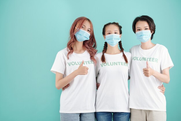 Jeunes femmes volontaires portant des masques de protection étreignant et montrant le pouce levé