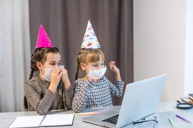 Jeunes filles portant un masque facial pendant la pandémie de Covid-19 ou de coronavirus le jour de leur anniversaire, assises à une table