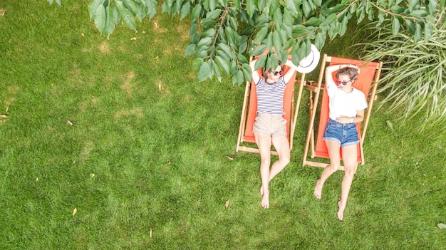 Les jeunes filles se détendent dans le jardin d'été dans des chaises longues sur l'herbe, les amies s'amusent à l'extérieur