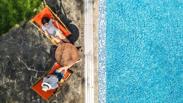 Les jeunes filles se détendent près de la piscine dans des transats transats femmes amis s'amusent