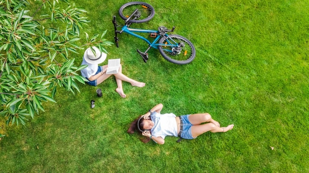 Jeunes filles à vélo dans le parc, écoutant de la musique avec des écouteurs et lisant un livre, deux étudiantes