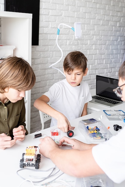 Jeunes garçons et enseignant s'amusant à construire des voitures-robots ensemble à l'atelier