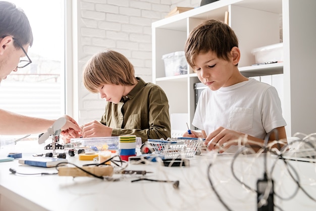 Jeunes garçons et enseignant s'amusant à construire des voitures-robots ensemble à l'atelier