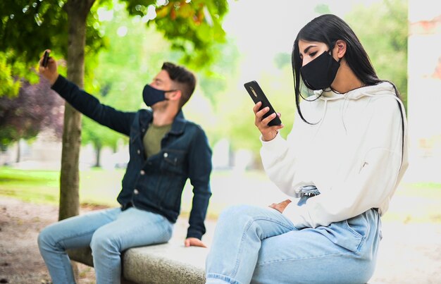 Les jeunes gardent une distance sociale en raison du coronavirus tout en utilisant leur téléphone à l'extérieur dans un parc