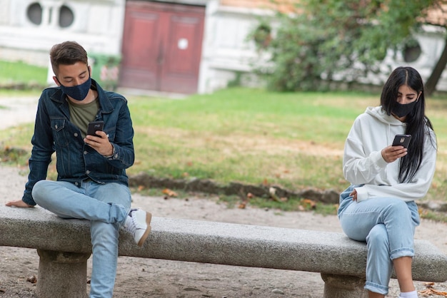 Les jeunes gardent une distance sociale en raison du coronavirus tout en utilisant leur téléphone à l'extérieur