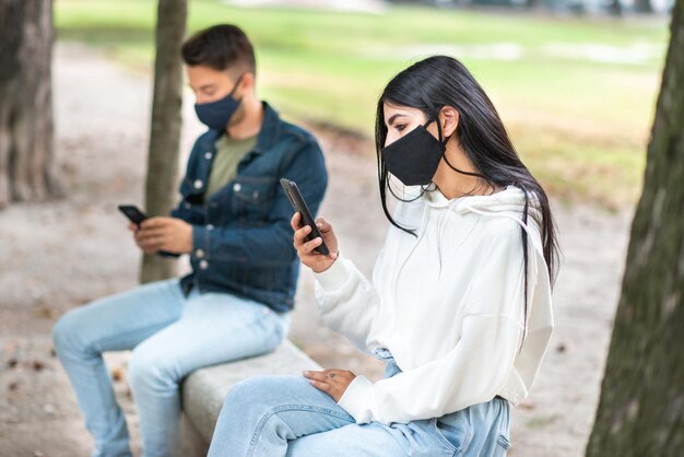 Les jeunes gardent une distance sociale en raison du coronavirus tout en utilisant leur téléphone à l'extérieur