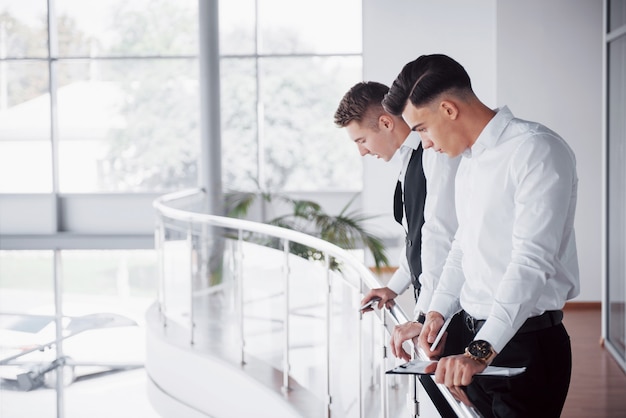 Les jeunes gens d'affaires à la recherche de documents et de produits debout à la balustrade du bureau.