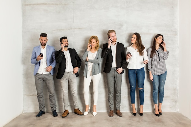 Jeunes gens d&#39;affaires avec téléphone portable debout près du mur