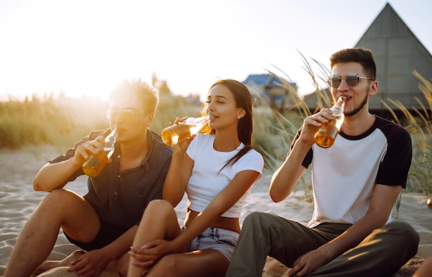 Des jeunes gens assis ensemble sur la plage buvant de la bière Un groupe d'amis applaudit avec des bières sur la plague
