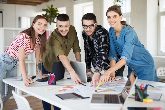 Jeunes gens créatifs souriants regardant joyeusement à huis clos travaillant avec un ordinateur portable Groupe de gars sympas travaillant sur un nouveau projet tout en passant du temps dans un bureau moderne