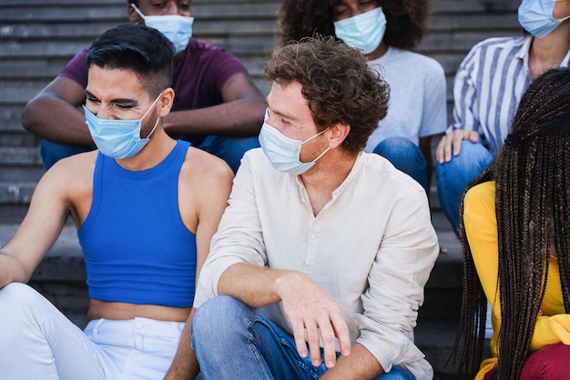 Jeunes gens divers riant ensemble portant un masque de sécurité en plein air dans la ville - Focus sur le visage de l'homme central