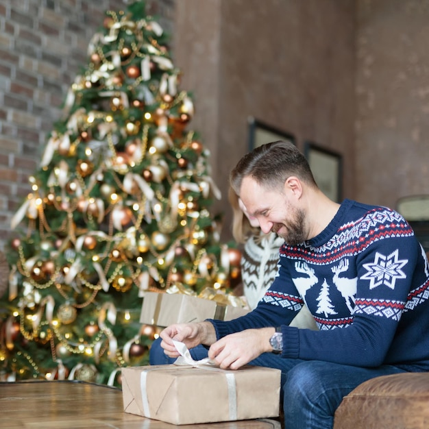 Jeunes gens heureux ouvrant des coffrets cadeaux de Noël assis près de l'arbre de Noël