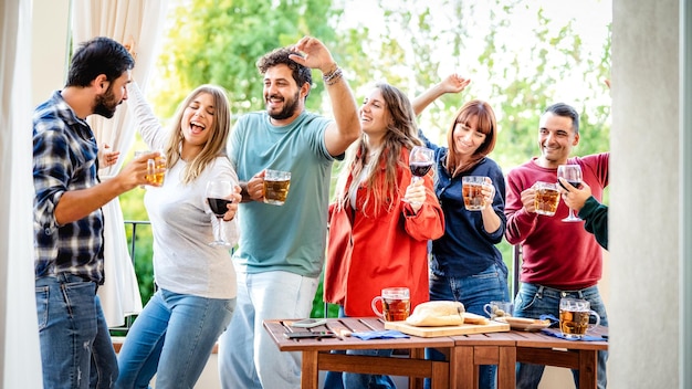 Jeunes gens s'amusant à manger à la maison dîner sur le balcon Amis heureux buvant de la bière et du vin dans un lieu de toit alternatif chic ensemble Concept de style de vie à manger sur un filtre vif et lumineux