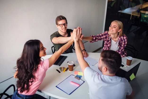 Des jeunes heureux et gais s'asseoir autour de la table et garder les mains ensemble