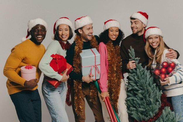 Photo des jeunes heureux portant un arbre de noël et divers ornements sur le fond du studio