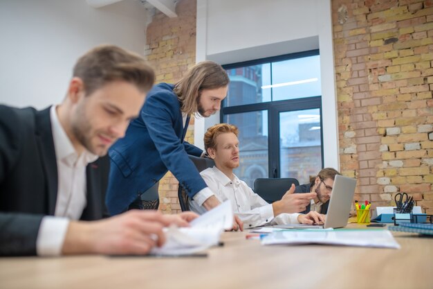 Les jeunes hommes adultes au bureau en cours de travail sur ordinateur portable et avec des papiers