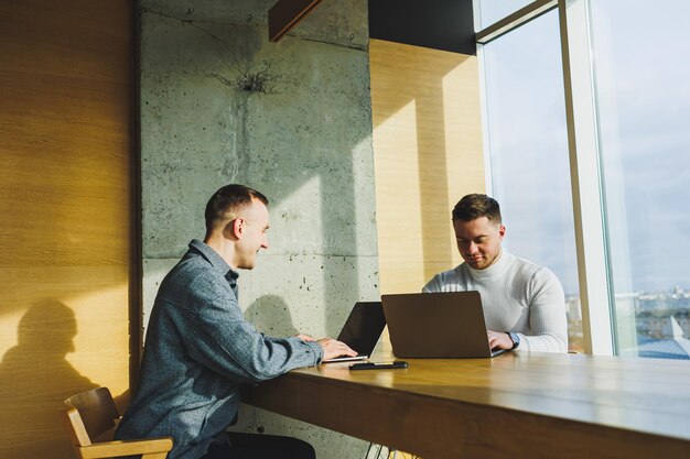 Jeunes hommes d'affaires deux collègues masculins travaillant avec un ordinateur portable au bureau Deux hommes d'affaires collaborent dans un espace de travail moderne Deux jeunes hommes d'affaires travaillent dans un bureau lumineux