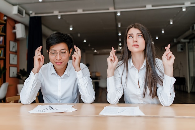 Jeunes hommes d'affaires du millénaire espérant et priant avec les doigts croisés dans le bureau