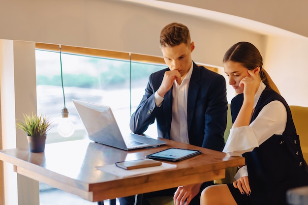 Jeunes hommes d&#39;affaires, garçon et fille, travaillent avec un ordinateur portable, une tablette et des notes au café