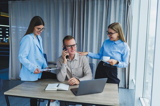 Jeunes hommes d'affaires prospères riant tout en collaborant sur un nouveau projet au bureau Groupe de divers hommes d'affaires utilisant un ordinateur portable tout en travaillant ensemble dans un espace de travail moderne