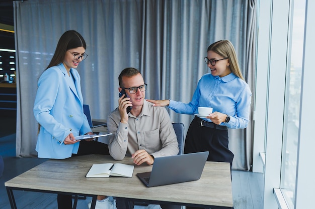 Jeunes hommes d'affaires prospères riant tout en collaborant sur un nouveau projet au bureau Groupe de divers hommes d'affaires utilisant un ordinateur portable tout en travaillant ensemble dans un espace de travail moderne