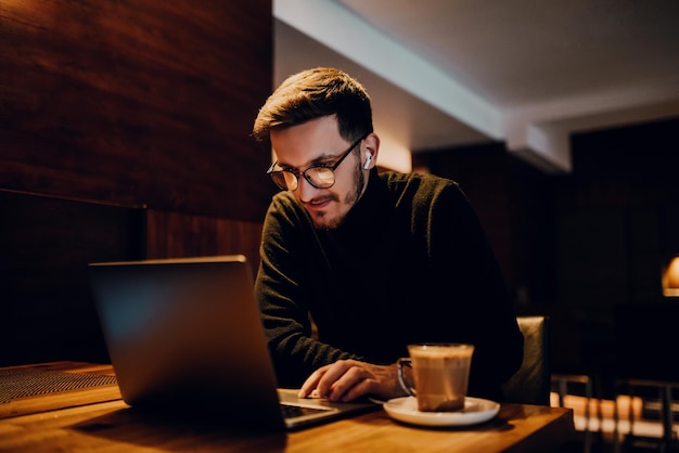 Jeunes hommes d'affaires utilisant un ordinateur portable pour une réunion en ligne assis dans un café moderne.