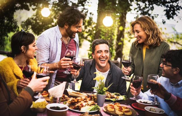 Jeunes hommes et femmes s'amusant à boire au restaurant de vin Concept de style de vie de nourriture et de boisson sur les personnes d'âge mixte profitant du temps ensemble au patio de la villa Filtre chaud avec halo de lumières de guirlande d'ampoules