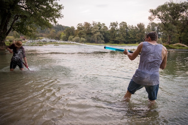 jeunes hommes s'amusant avec des pistolets à eau tout en s'éclaboussant au coucher du soleil sur la rivière