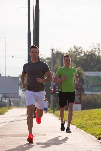 les jeunes hommes sportifs aiment courir pendant que le soleil se lève sur la ville