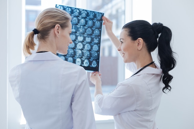 Les jeunes infirmières souriantes et décontractées travaillant au cabinet de roentgen tout en examinant l'image aux rayons x du cerveau et en discutant