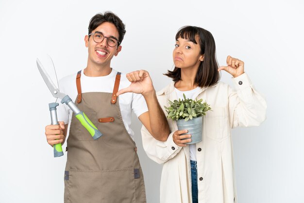 Jeunes jardiniers de race mixte tenant une plante et un sécateur isolés sur fond blanc fiers et satisfaits de l'amour vous-même concept