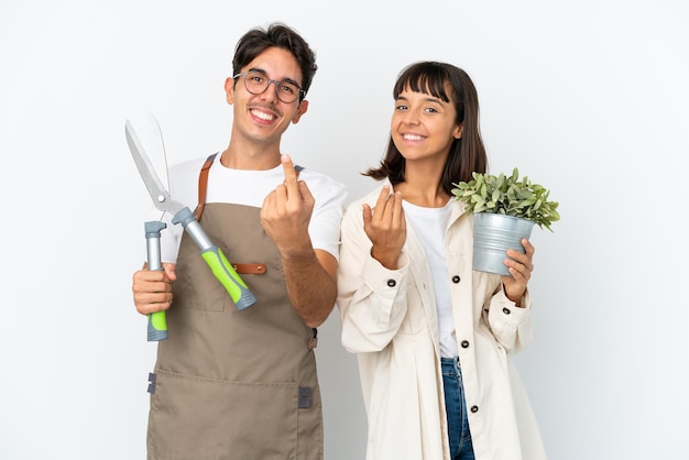 Jeunes jardiniers de race mixte tenant une plante et un sécateur isolés sur fond blanc invitant à venir avec la main Heureux que vous soyez venu