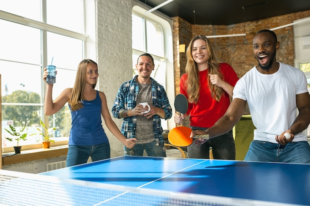 Jeunes jouant au tennis de table sur le lieu de travail, s'amusant. Des amis en tenue décontractée jouent au ping-pong ensemble par beau temps. Concept d'activité de loisirs, sport, amitié, teambuilding, travail d'équipe.