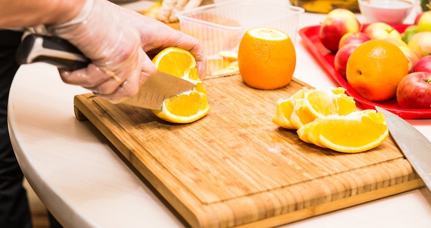 Jeunes mains propres de chef coupant l'orange sur la table