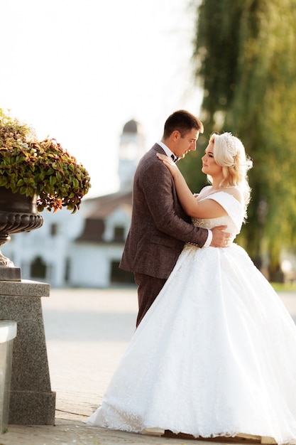 Jeunes mariés au jour du mariage en marchant à l'extérieur sur la nature du printemps. Couple nuptial, heureux jeune femme et homme embrassant dans un parc verdoyant. Couple de mariage aimant en plein air.