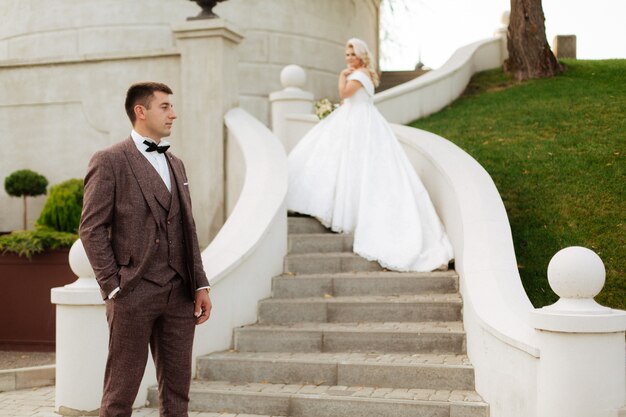 Jeunes mariés au jour du mariage en marchant à l'extérieur sur la nature du printemps. Couple nuptial, heureux jeune femme et homme embrassant dans un parc verdoyant. Couple de mariage aimant en plein air.