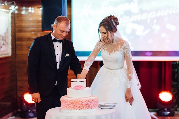 Les jeunes mariés coupent et goûtent joyeusement le gâteau de mariage