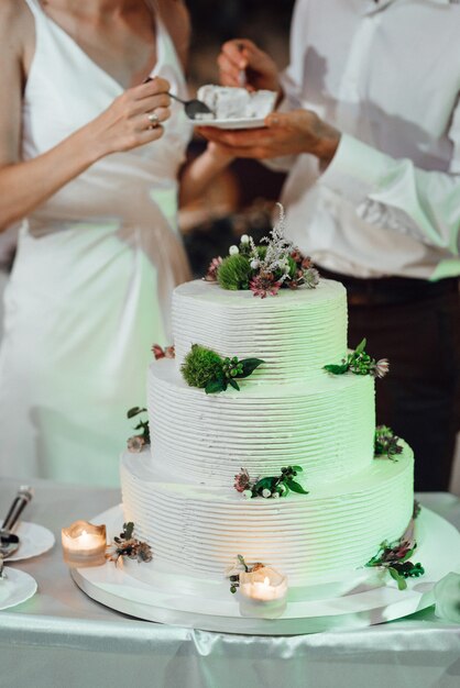 Les jeunes mariés coupent, rient et goûtent joyeusement le gâteau de mariage