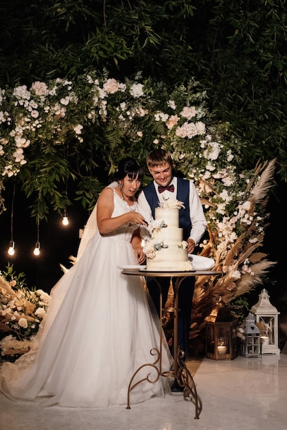 Les jeunes mariés coupent, rient et goûtent joyeusement le gâteau de mariage