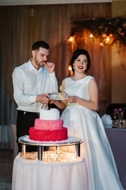 Les jeunes mariés coupent, rient et goûtent joyeusement le gâteau de mariage