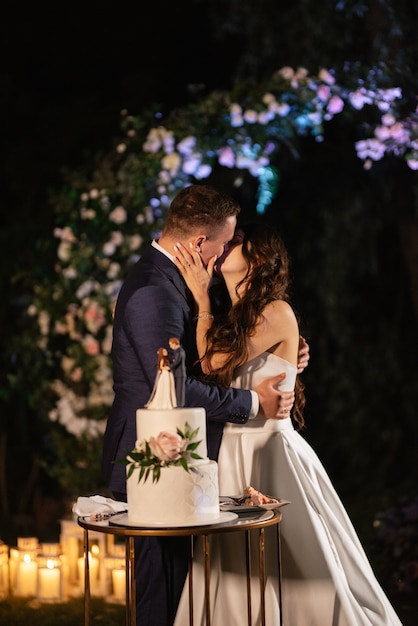 Les jeunes mariés coupent, rient et goûtent joyeusement le gâteau de mariage