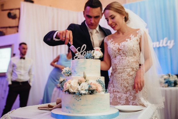 Les jeunes mariés coupent, rient et goûtent joyeusement le gâteau de mariage