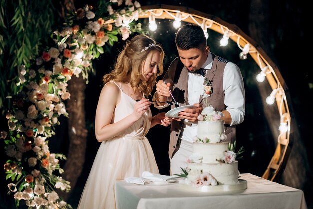 Les jeunes mariés coupent, rient et goûtent joyeusement le gâteau de mariage